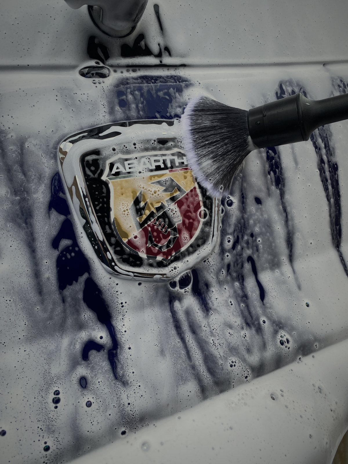 Detailing brush cleaning an Abarth badge